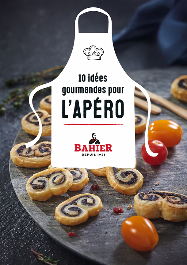 Recette-Bahier-Livret Couverture d’un livret de recettes Bahier de 16 pages consacré à l’apéritif. Sur un fond sombre et élégant, une planche en ardoise présente des feuilletés apéritifs en forme de spirales garnies, accompagnés de tomates cerises rouges et jaunes. Au centre de l’image, une illustration de tablier blanc contient le titre « 10 idées gourmandes pour l’apéro ». En bas du tablier figure le logo Bahier avec la mention « Depuis 1941 ». L’ensemble évoque la convivialité et la gourmandise autour de la charcuterie. Réalisé par l'agence A tribu - Le Mans